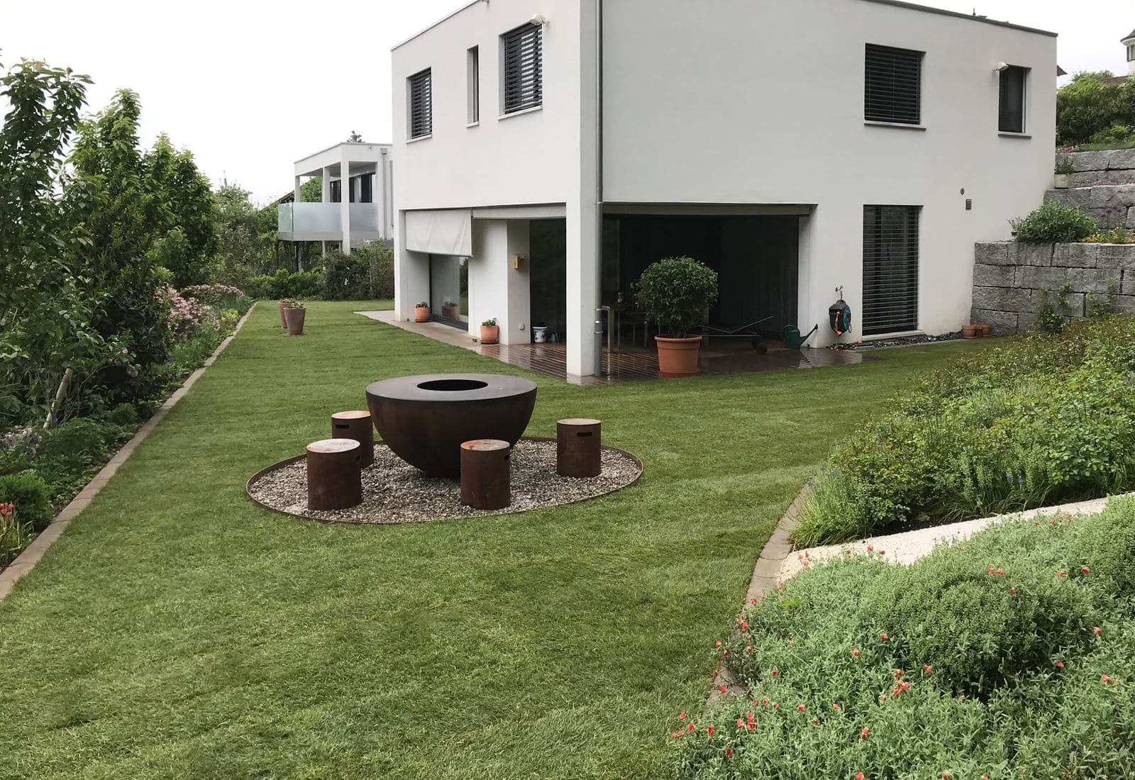 Neuer Rasen mit Feuerstelle vor einem modernen Haus