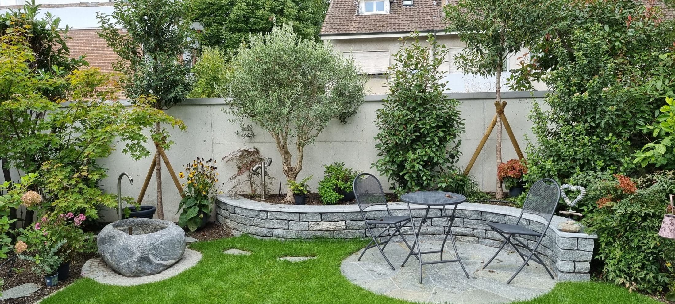 Sitzplatz mit runder Natursteinmauer, Olivenbaum und Bepflanzung
