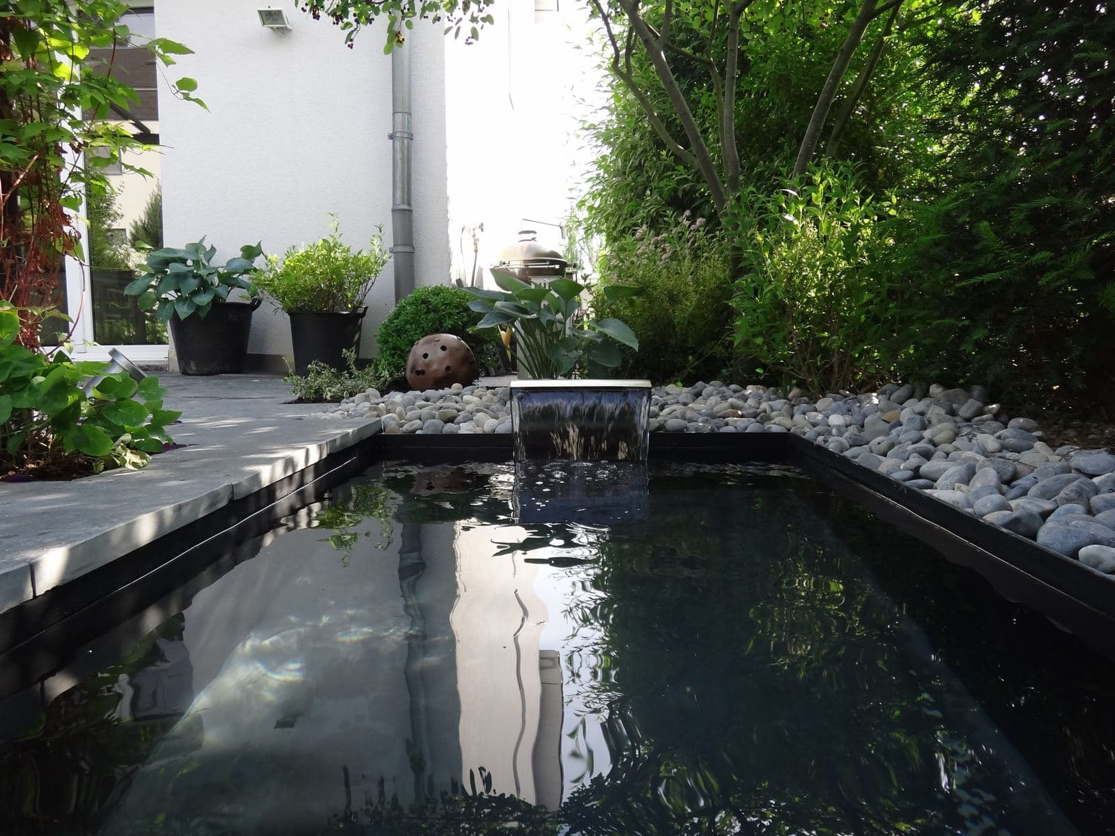 Modernes Wasserbecken mit Wasserfall und Kieselufer